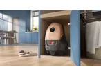 Vacuum cleaner stored in a wooden cabinet, with slippers on a wooden floor in a modern kitchen.