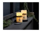 Two LED candles with star charms and remote control on a dark shelf with greenery.