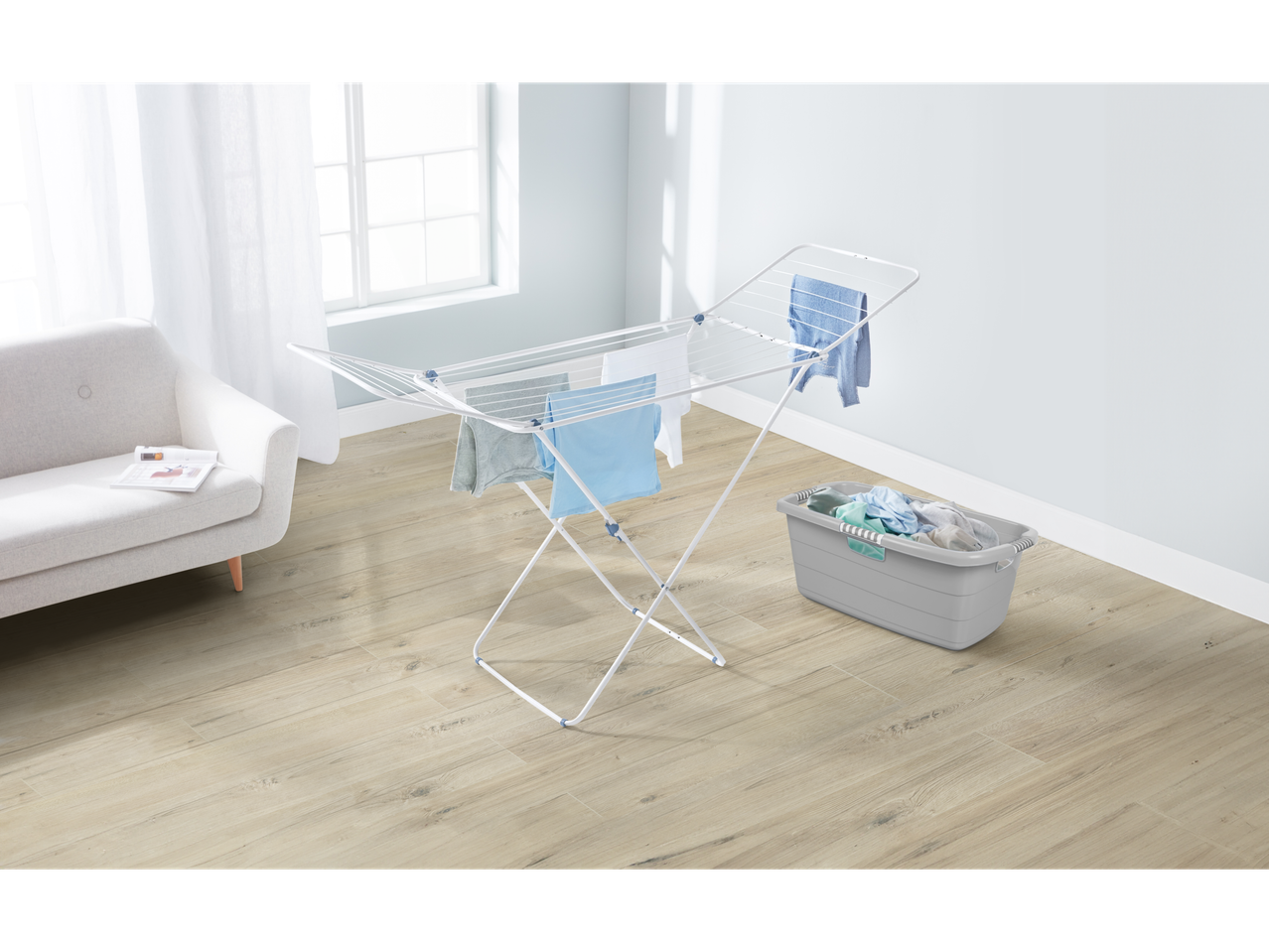 Ein weißer Wäscheständer mit Wäsche steht in einem hellen Raum mit hellem Holzboden.