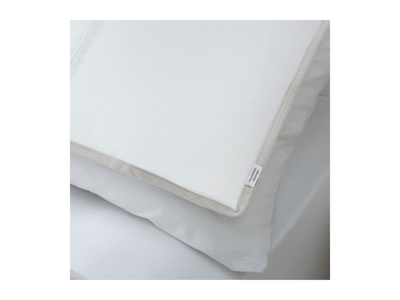 White pillow with a light grey trim and a small purple label, resting on a white sheet.