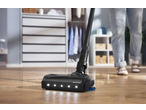 Cordless vacuum cleaner with Aqua Spin Mop head cleaning a wooden floor with visible dirt.