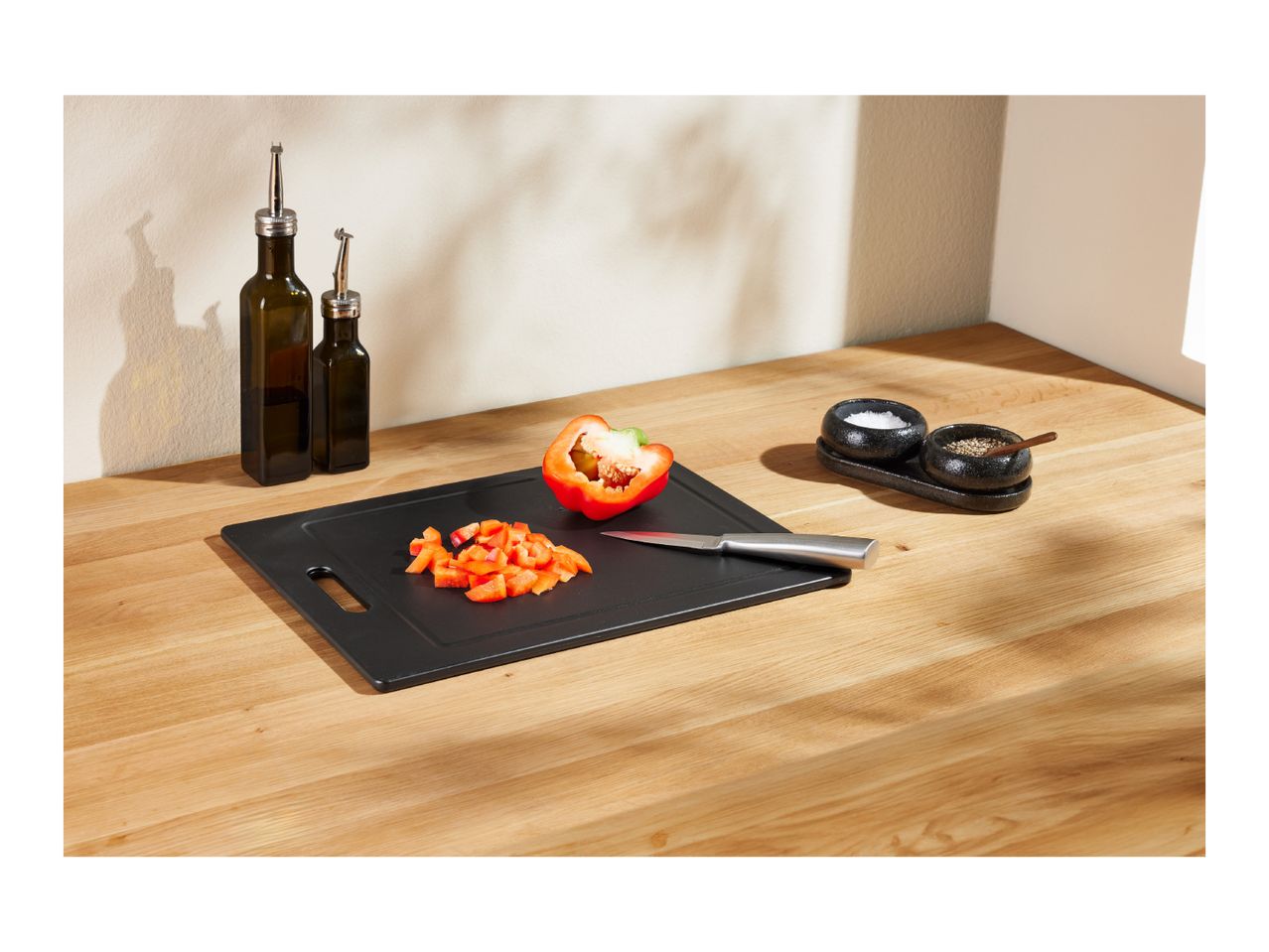 Chopped red bell pepper on a black cutting board with a knife, oil bottles, and spices.
