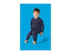 Smiling boy in dark blue pajamas with construction vehicle print, sitting on a blue cube.