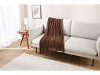 Uma sala de estar aconchegante com um sofá claro, uma manta marrom e uma mesa lateral.