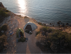 Duas pessoas acampando à beira-mar, uma em saco de dormir Crivit, a outra em barraca.