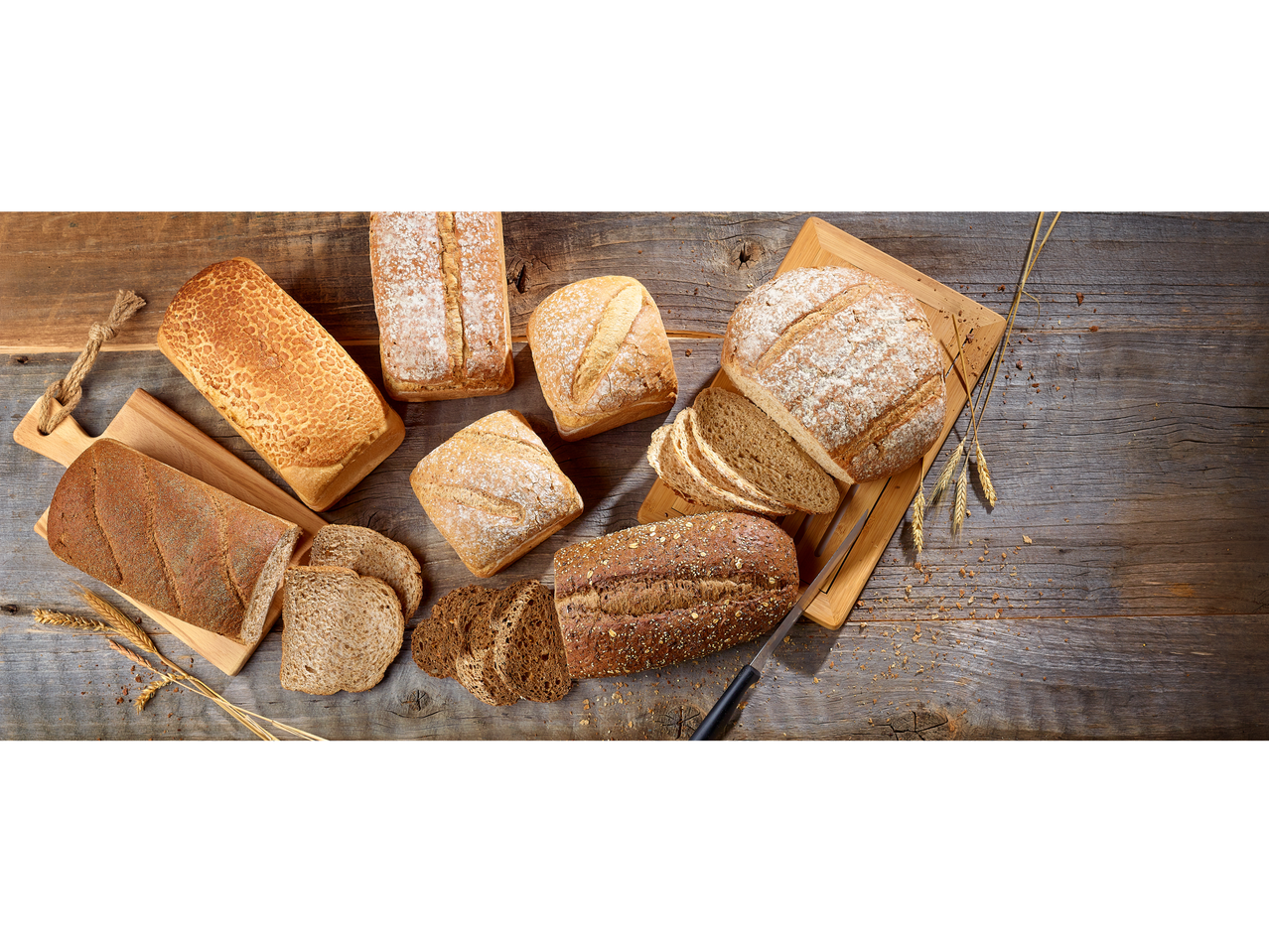 Assortiment de pains : pain blanc, pain complet et pain aux céréales sur une table en bois.