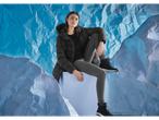 Woman in black puffer jacket, grey leggings, and black winter boots, sitting on a blue block.