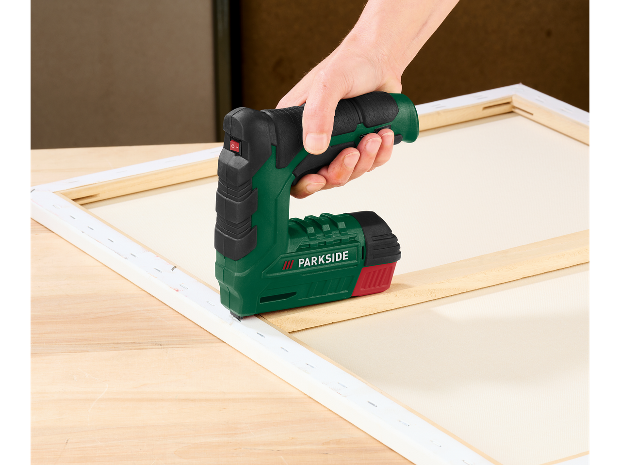 O mână folosește un capsator electric pentru a fixa o pânză pe un cadru de lemn.