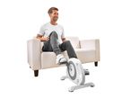 Man in white t-shirt and grey sweatpants using a Crivit mini exercise bike while sitting on a sofa.