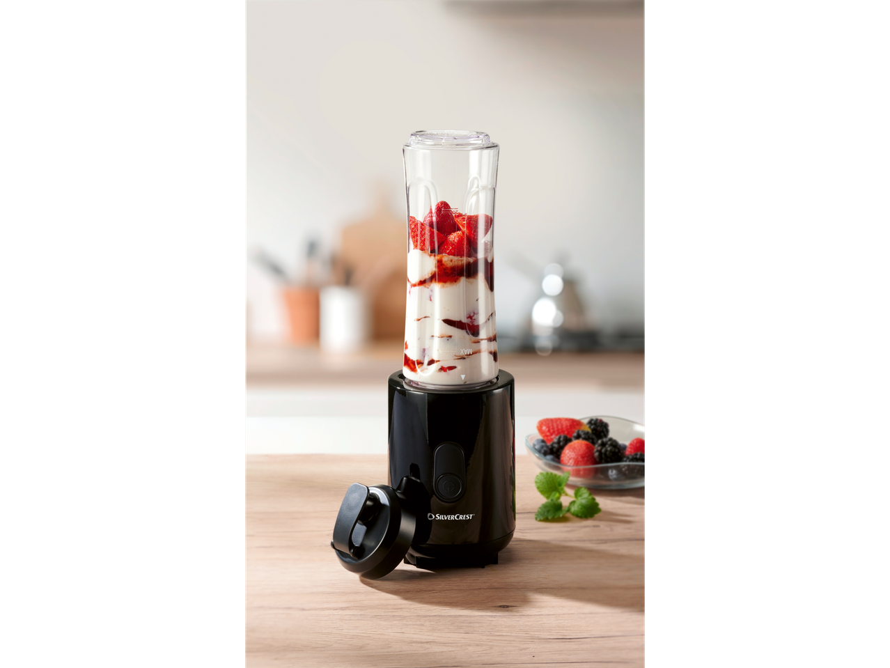 A SilverCrest personal blender sits on a wooden counter with fresh berries nearby, ready to make a smoothie.