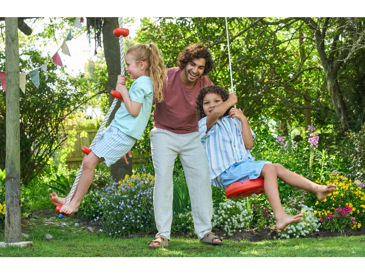 Father and children playing with Lupilu swings outdoors.