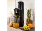 Black slow juicer making orange juice, with pineapple, orange, and grapes nearby.