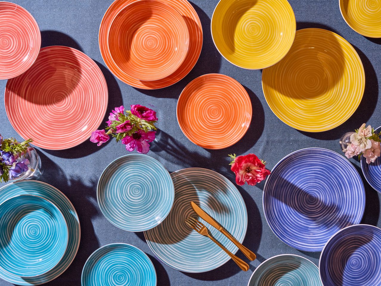 Un assortimento di piatti e ciotole Tognana colorati con motivi a spirale su un tavolo blu.