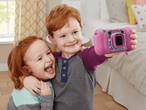 Zwei rotblonde Kinder machen mit einer pinkfarbenen VTech Kidizoom-Kamera ein Selfie.