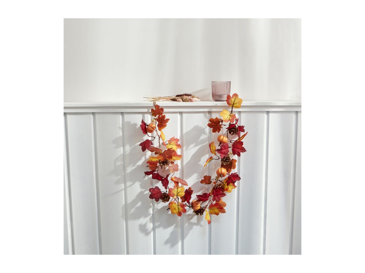 Autumn garland with leaves, pumpkins, and pinecones draped over a white shelf.