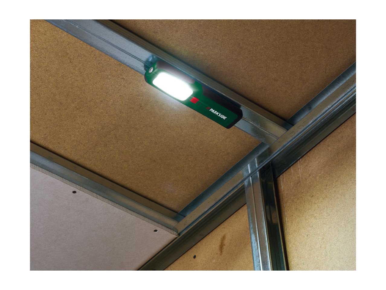 A bright work light attached to a metal stud frame, illuminating a wooden panel.