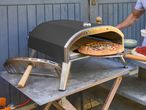 Outdoor pizza oven with a pizza being cooked, next to pizza ingredients.