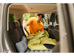 Um homem coloca um saco de dormir e um colchão inflável no porta-malas de um carro.