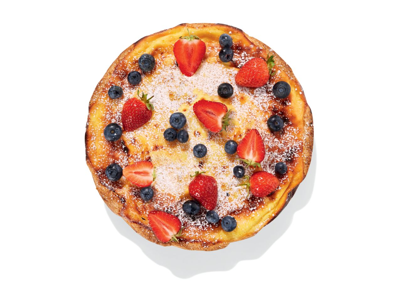 A round Dutch baby pancake topped with strawberries, blueberries, and powdered sugar.