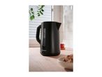 Black kettle on a wooden kitchen counter with a cup of tea and cookies in the background.