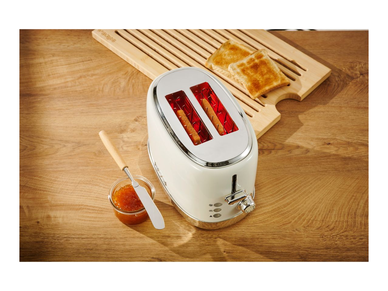Cream toaster with two slices of toast, jam, and a wooden cutting board.