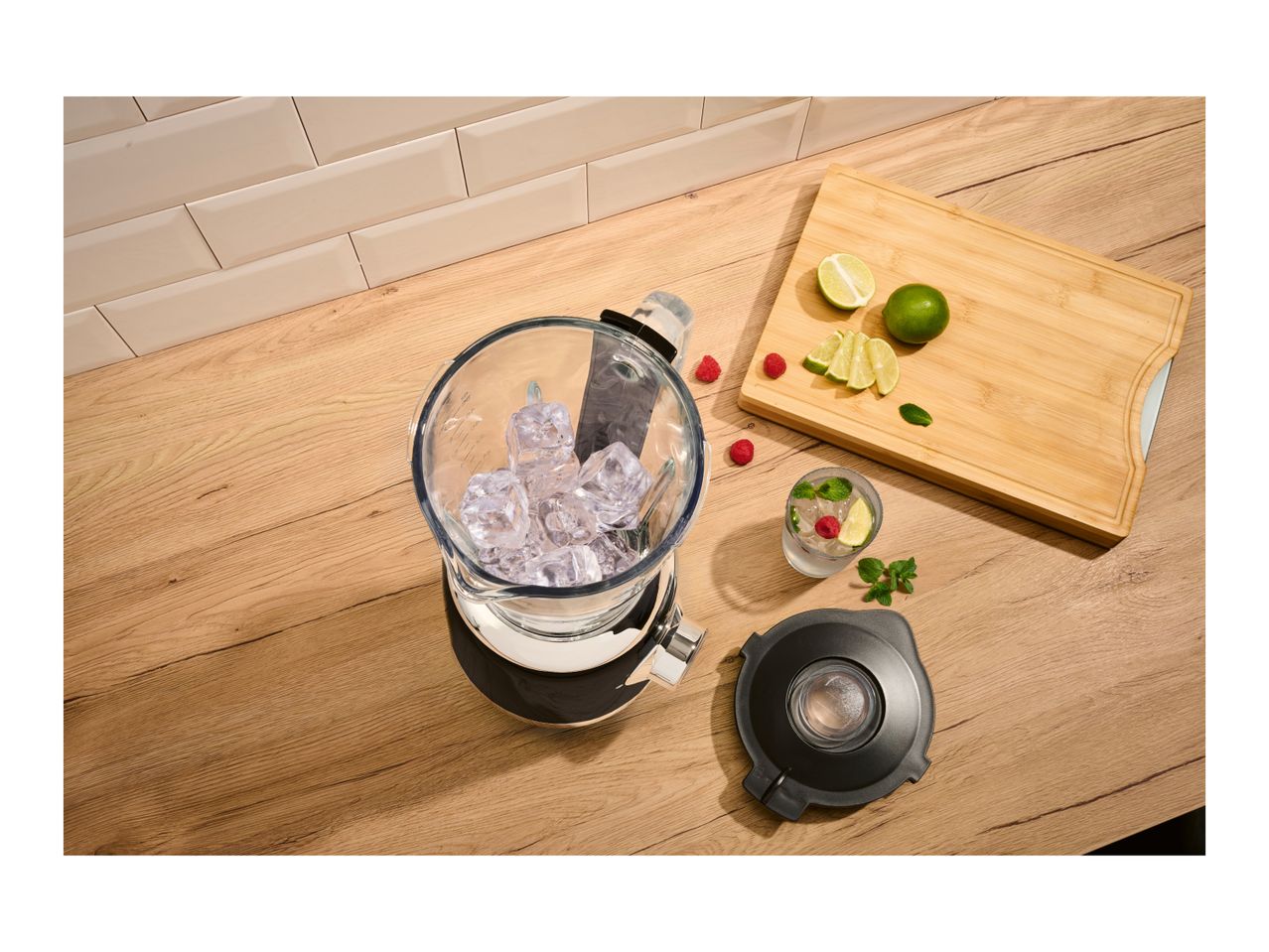 A black and silver blender filled with ice cubes on a wooden countertop next to fresh limes.