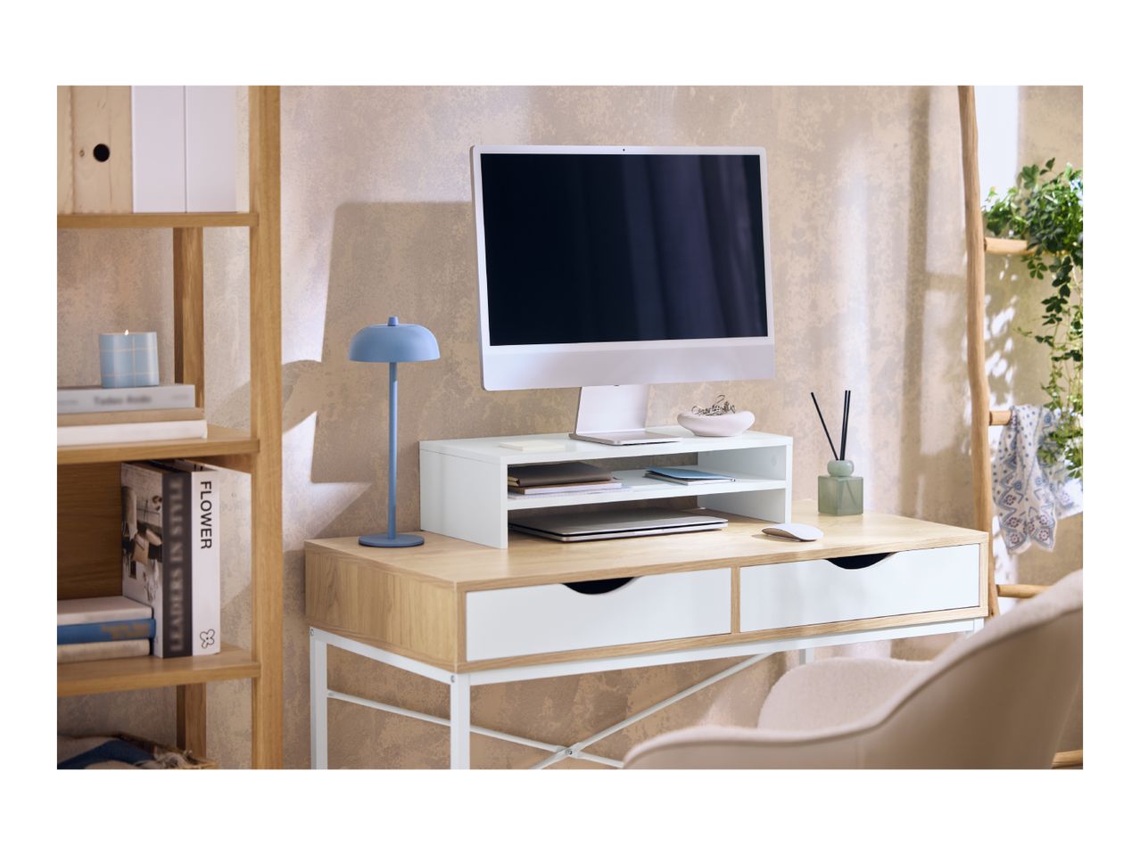 Home office desk with a computer, monitor stand, blue lamp, and wooden shelving unit.