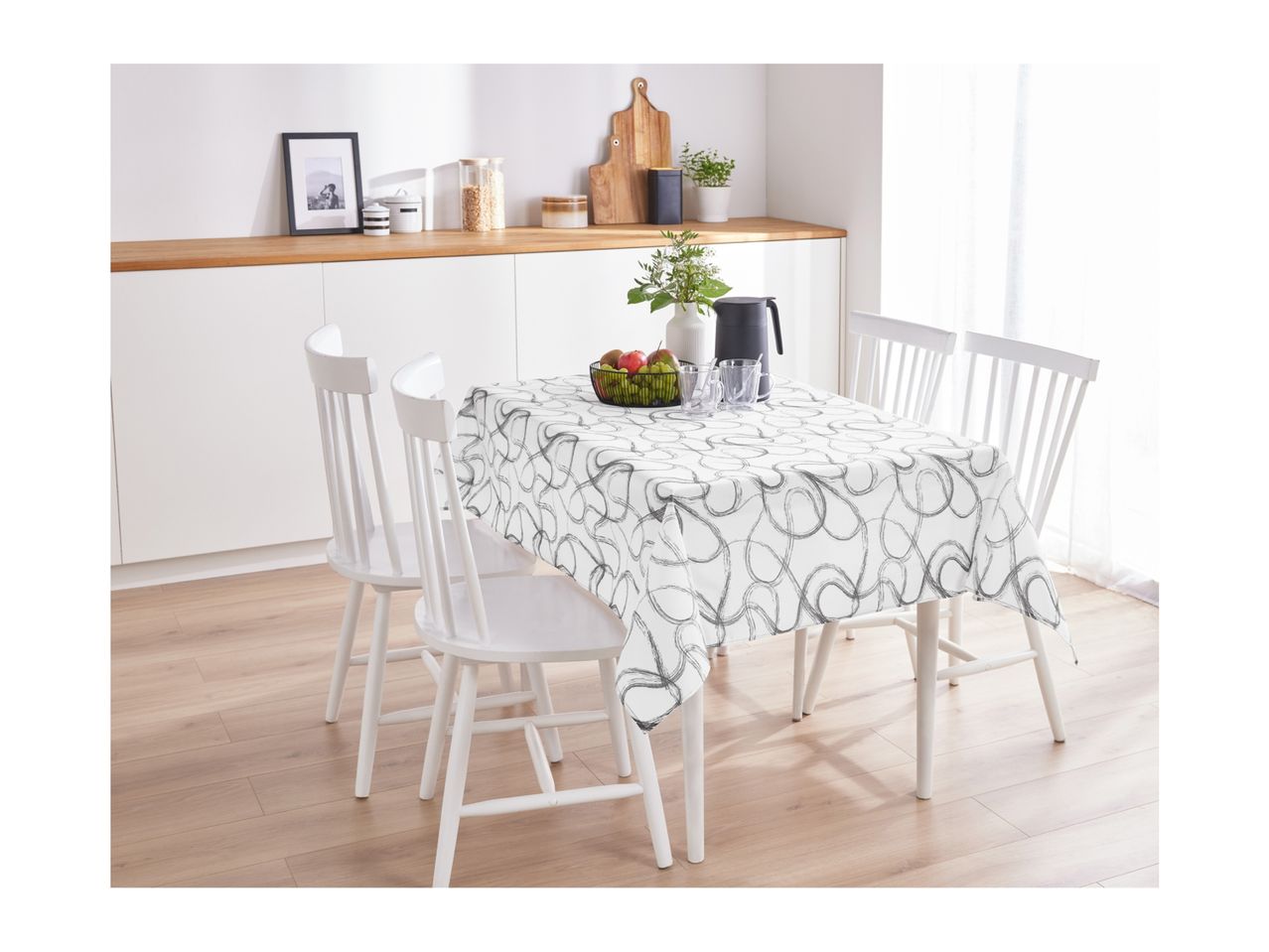 Dining table with a white tablecloth featuring a grey abstract pattern, surrounded by white chairs.