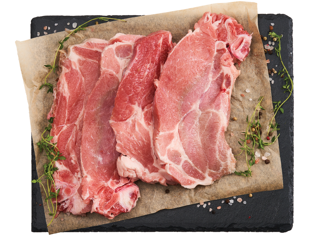 Сурови свински пържоли с мащерка и подправки върху хартия за печене на черен фон.