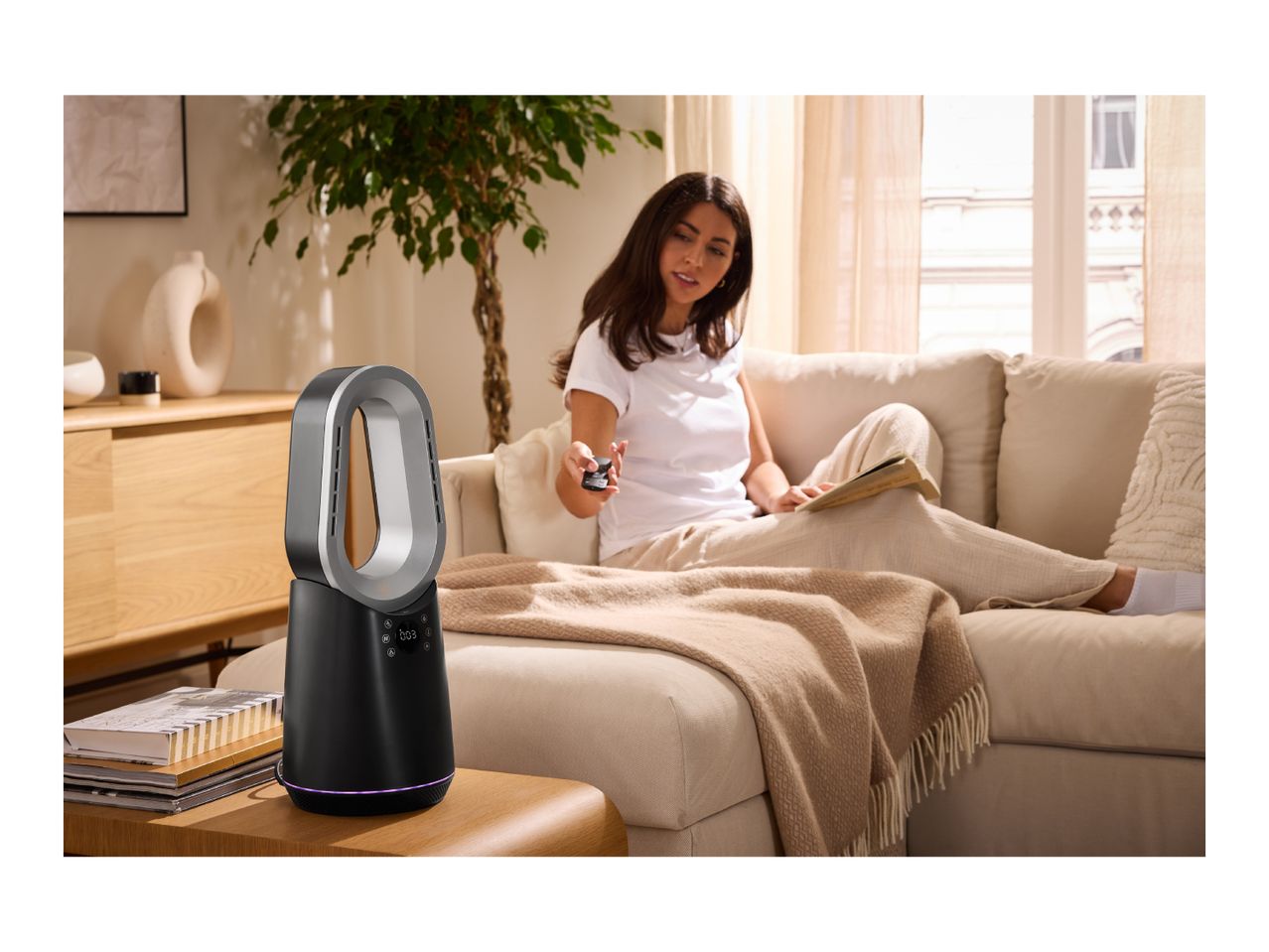 Woman on sofa with remote control, next to a modern bladeless fan on a side table.