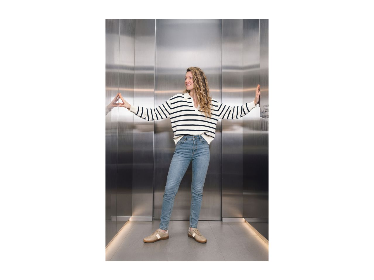 Woman in striped sweater, jeans, and sneakers in an elevator.