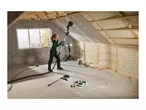 Woman sanding drywall in an attic with insulation, using a long-reach sander.