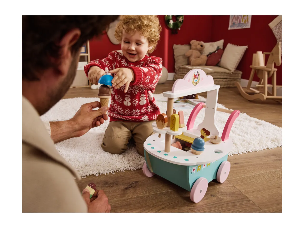 A child and adult playing with a wooden toy ice cream cart on a rug.