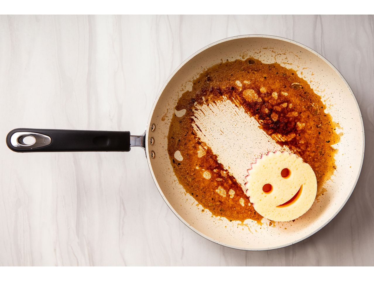 A smiley Scrub Mommy Sponge cleaning a pan.