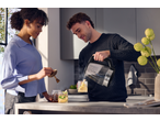 Man pouring water from a SILVERCREST® Colour Changing Glass Kettle into a mug, woman adding honey.