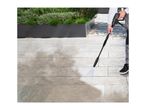 Person cleaning patio with a pressure washer, showing before and after cleaning.