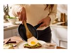 A person serving a fried egg from a frying pan onto avocado toast.