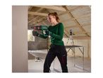 Woman drilling into a wall with a rotary hammer, wearing safety glasses and earplugs, in an attic under construction.