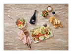 Balsamic vinegar bottle with a caprese salad, olives, figs, cheese, and bread on a wooden table.