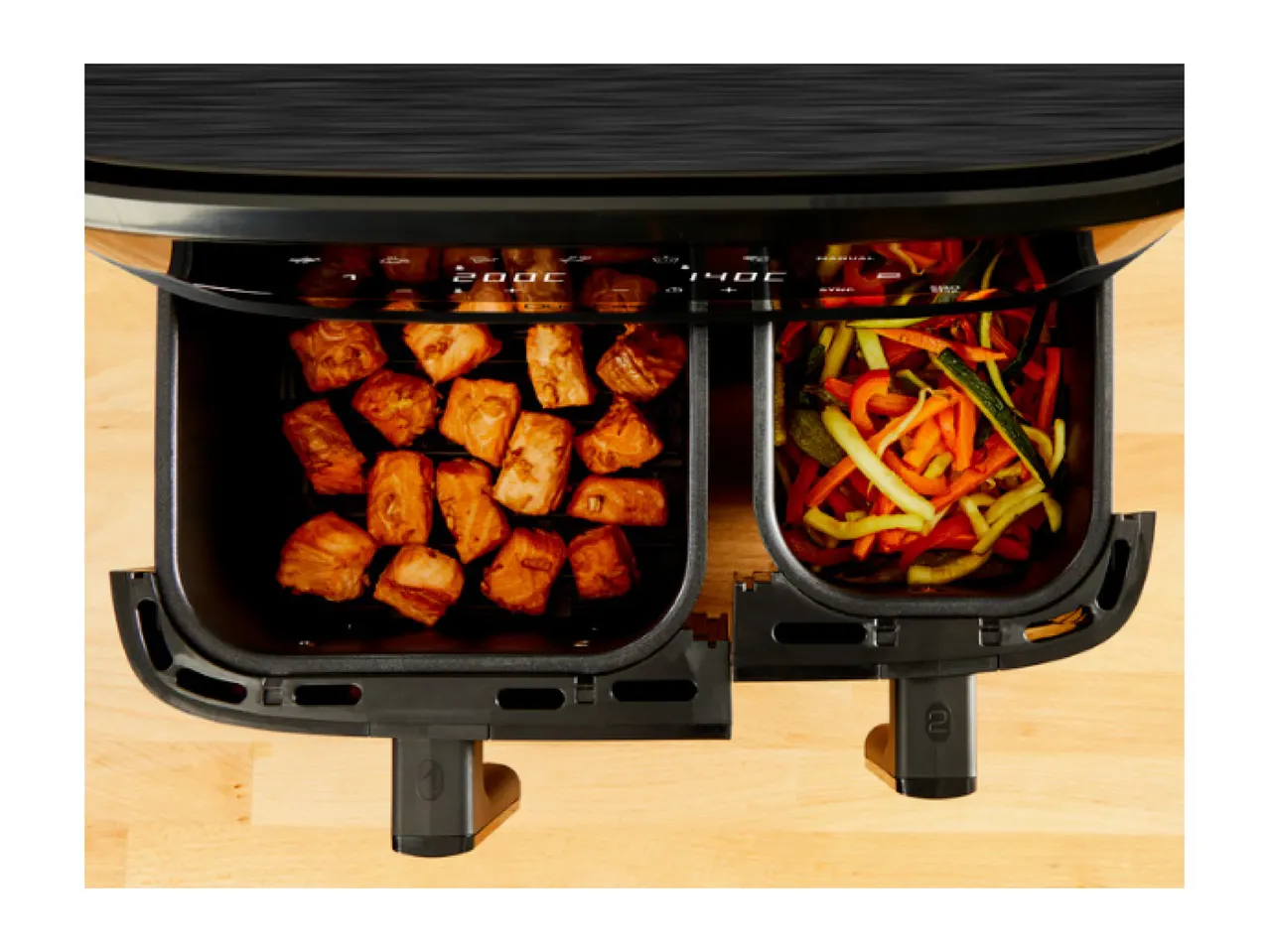Air fryer with two baskets, one with salmon pieces and the other with mixed vegetables.