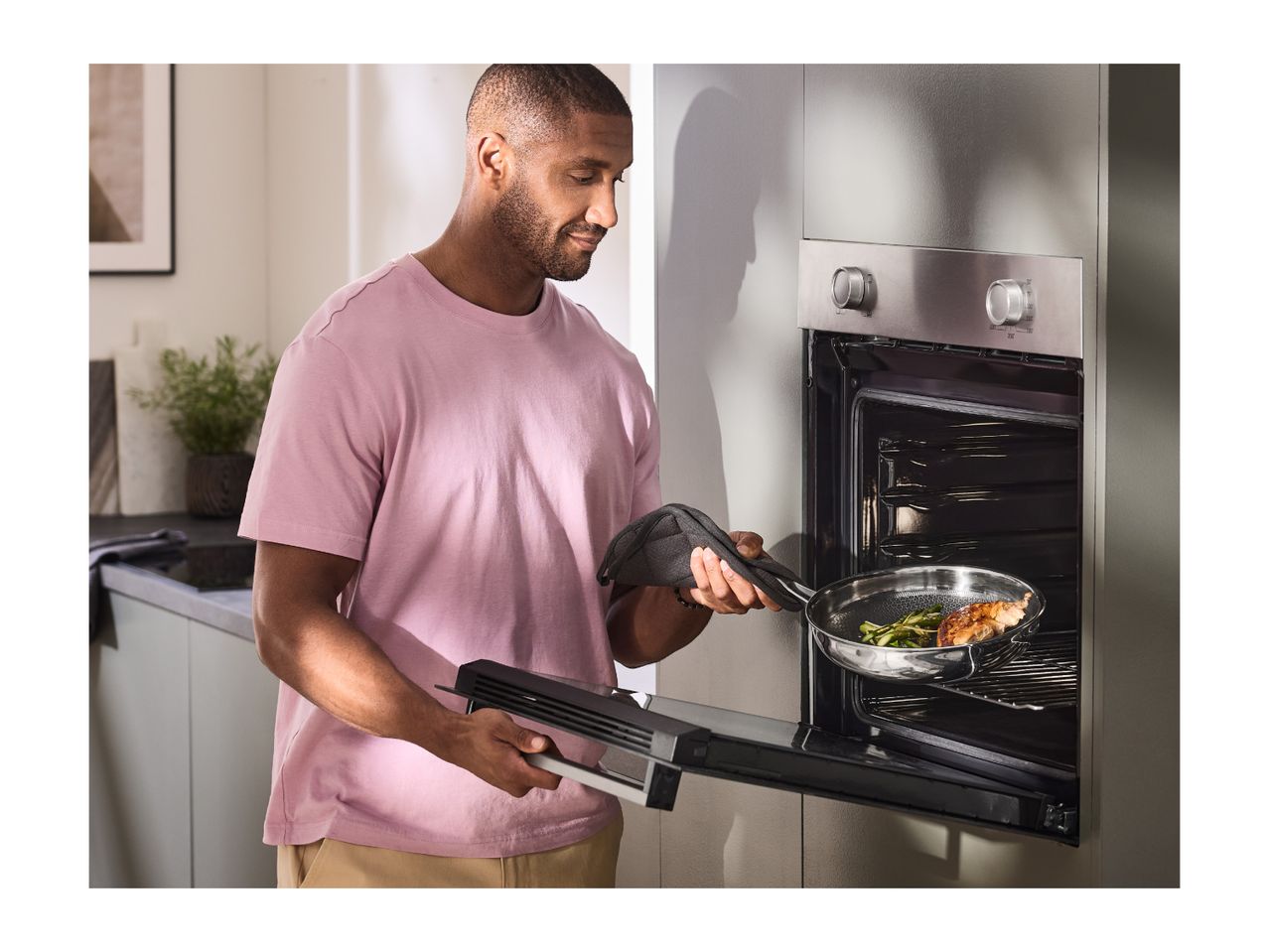 Man putting a pan with chicken and asparagus into an oven.