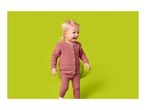 Happy baby in a pink knitted cardigan and trousers, standing next to a green ball.