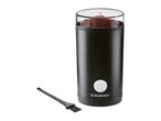Black electric coffee grinder with ground coffee inside and a cleaning brush beside it.