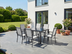 Conjunto de mobiliário de jardim com mesa e cadeiras cinzentas num pátio junto a uma casa branca com jardim.