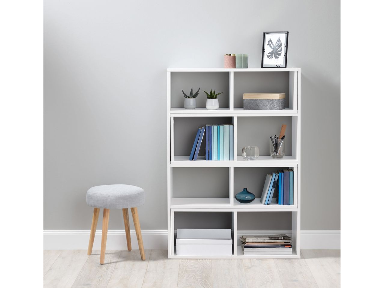 White cube storage unit with books and decorative items next to a gray stool.
