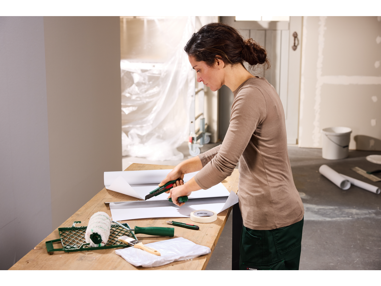 Femeie tăind hârtie cu un set de cuttere, cu unelte de pictură pe masă.