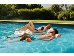 Duas pessoas a relaxar em redes de água CRIVIT na piscina num dia de sol.