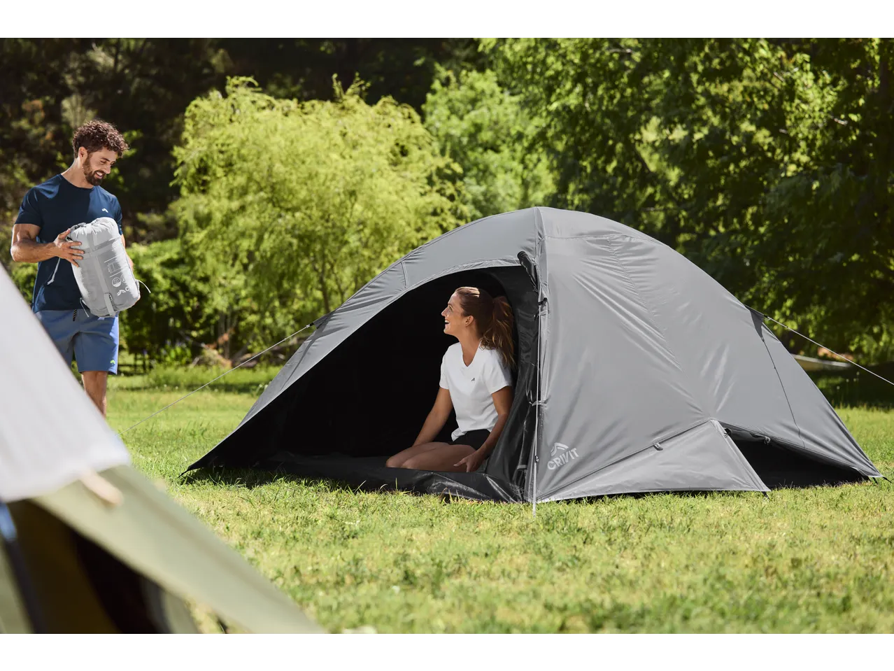 Man in CRIVIT sports top holding a sleeping bag, woman in a tent.