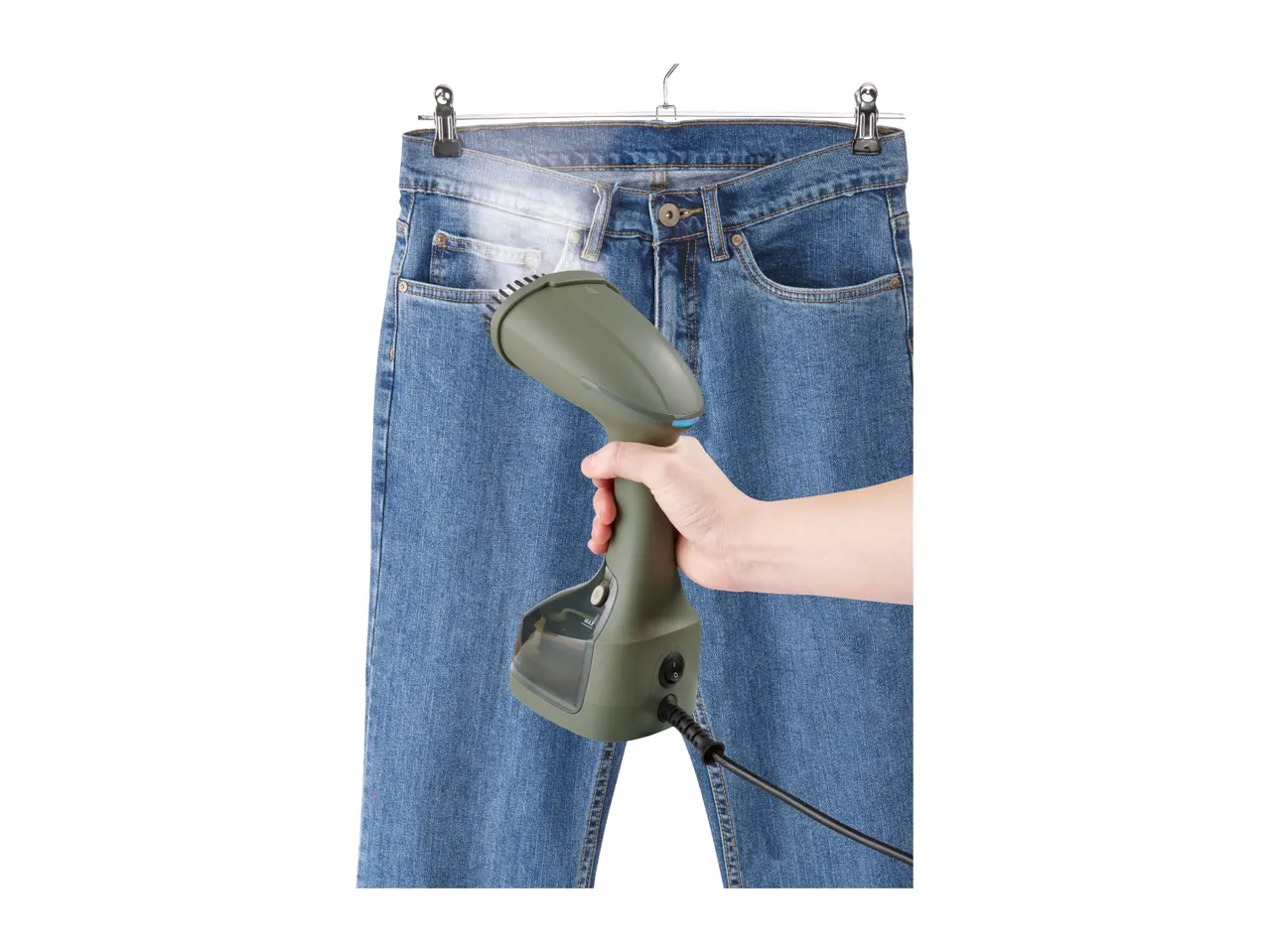 A hand holding a garment steamer to steam a pair of blue jeans hanging on a hanger.