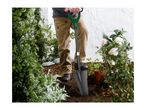 Person digging in a garden with a shovel, surrounded by plants and flowers.